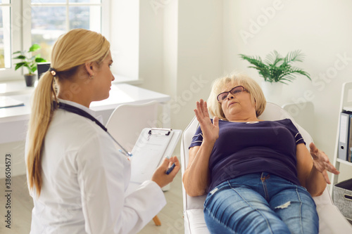 Senior female patient lying on a medical couch explains to a young woman doctor about her health.