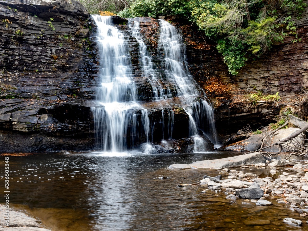 Fototapeta premium Muddy Falls in Swallow Falls State Park in Oakland, Maryland, the waterfall cascading and flowing down the side of the rocks in the autumn with leaves fallen in the water below.