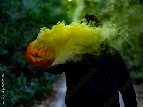 Hombre encapuchado con mascarilla sujetando una calabaza con humo de colores  photo