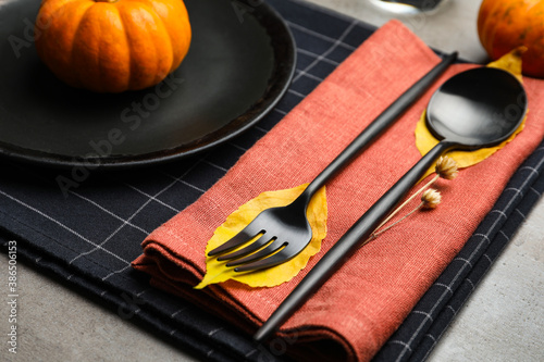 Seasonal table setting with pumpkins and autumn leaves on grey background, closeup