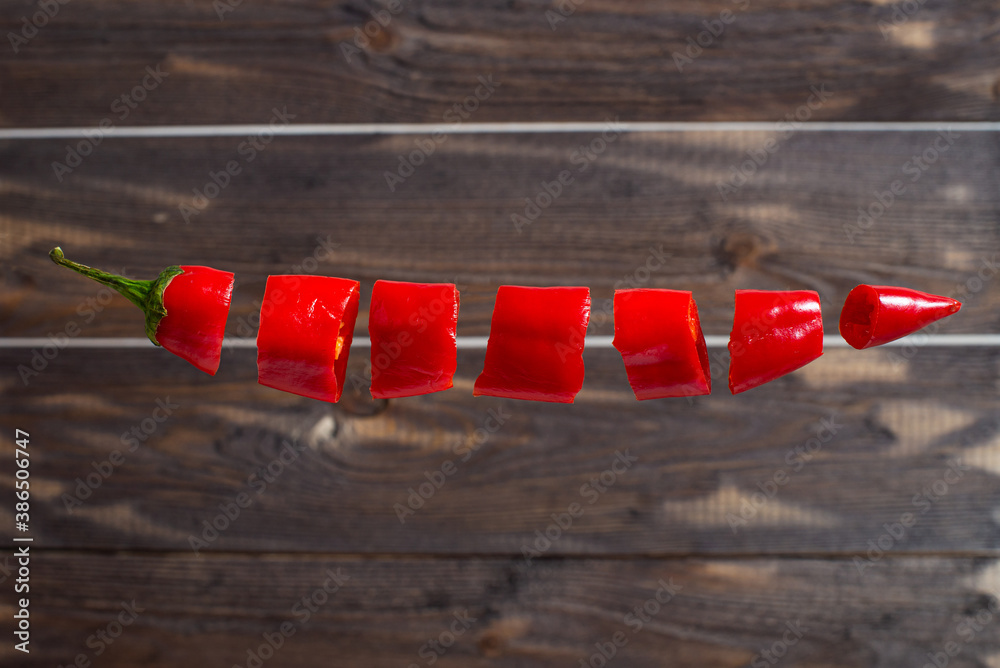 Chopped red chili peppers levitate in the air. Creative photo of a flying pepper on a dark wood background Chopped red chili peppers levitate in the air. Creative photo of a flying pepper on a dark wood background