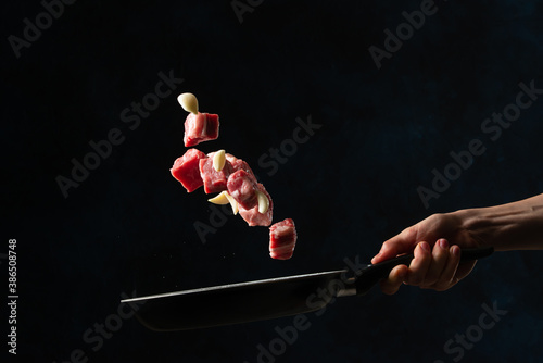 Chef's hand tossed chopped pork or beef with garlic in frying pan on black background. Backstage of cooking grilled meat for dinner. Food concept. Frozen motion. Asian cuisine.