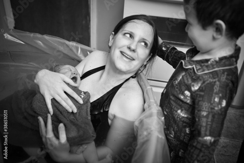Little Boy Comforting Mother Holding Newborn Baby in Birthing Pool After Home Birth