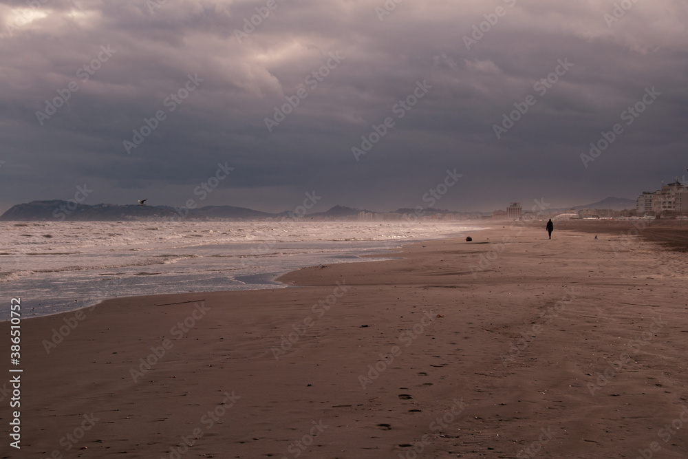 person walking alone on the beach on a cloudy and cold day