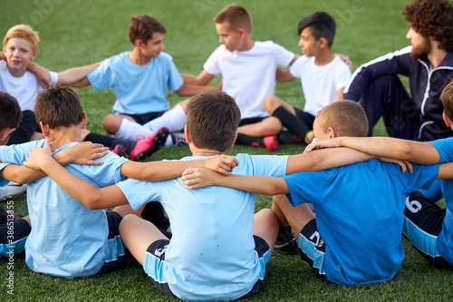 young team of sportive boys take a break during football competition, caucasian children talk, discuss, listen to trainer © Roman