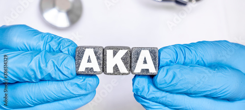 AKA Above the knee amputation - word from stone blocks with letters holding by a doctor's hands in medical protective gloves