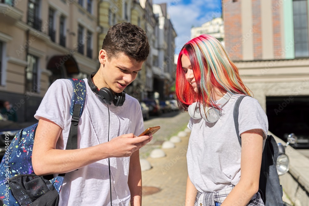 Teenagers students guy and girl with backpacks look in smartphone