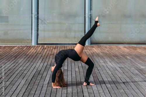 Young beautiful woman in a black outfit practicing yoga outdoors on a wooden floor