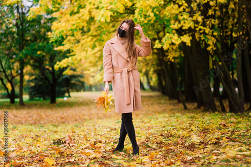 Young woman protecting from corona virus when walking in park. Autumn background. © Ivan Zelenin