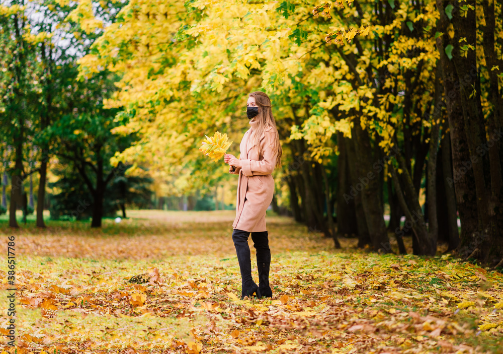 Young woman protecting from corona virus when walking in park. Autumn background.
