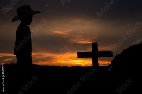 Sunset silhouette child cowboy standing at silhouetted cross grave