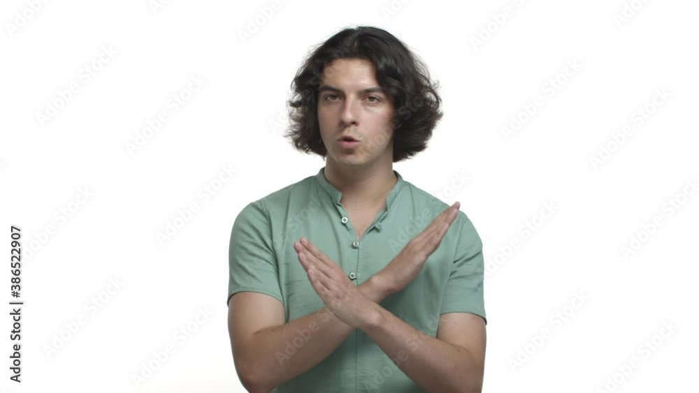 Displeased hispanic man with long dark hair, wearing casual clothing, saying no, disapprove something bad, shaking head and making cross, telling to stop, standing over white background Displeased hispanic man with long dark hair, wearing casual clothing, saying no, disapprove something bad, shaking head and making cross, telling to stop, standing over white background