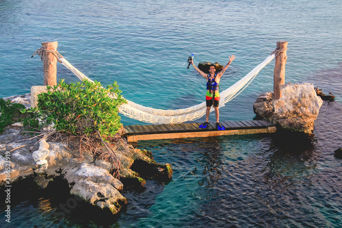 Young man with diving equipment and swimwear  in a hammock in the caribbean sea