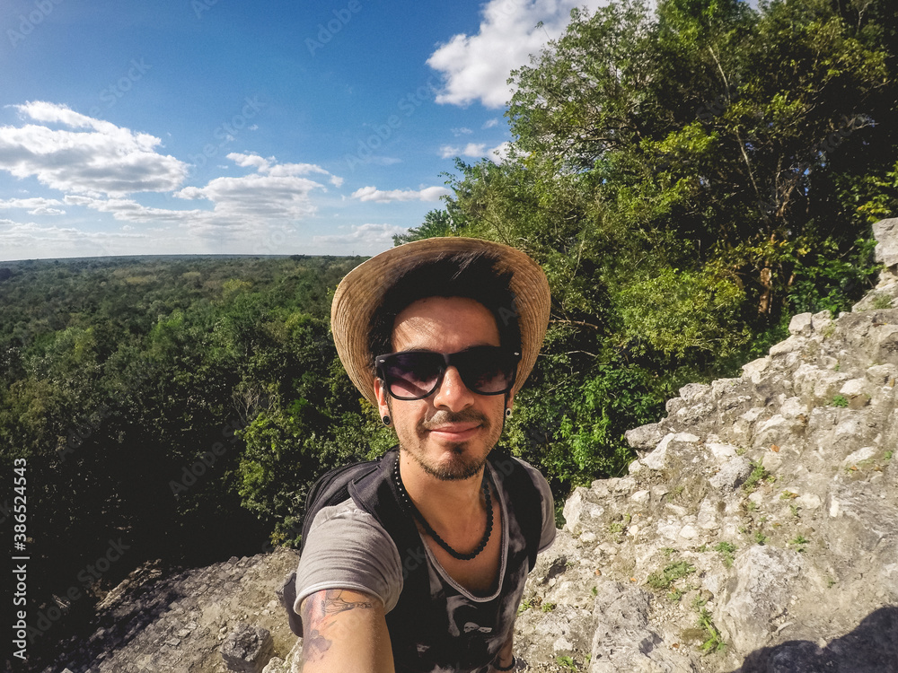Jungle view and handsome smiling guy with sunglass and hat at the stairs of the Nohoch Mul Mayan Pyramid, at Coba, Mexico