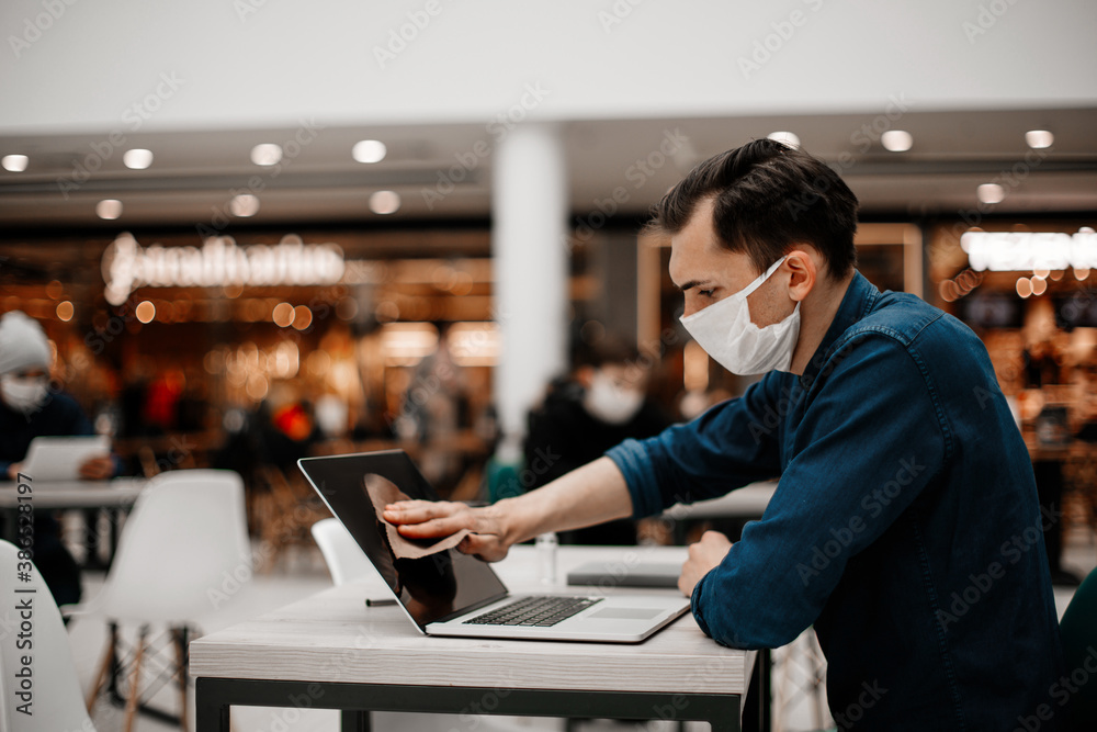 Fototapeta premium man in a protective mask wiping the laptop screen with antiseptic.
