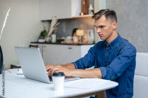 young man is working on a laptop in his kitchen.