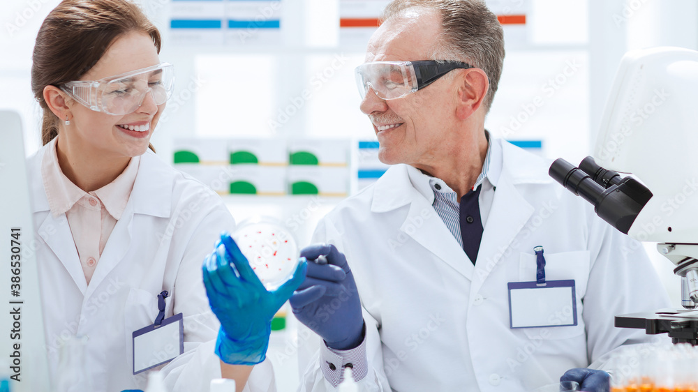 smiling scientists with a Petri dish sitting at a laboratory table.