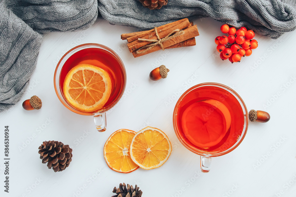 Cozy autumn flat lay composition. Top view on cup of tea, lemon, cinnamon, berries and cones on a white table near gray warm sweater. Cozy autumn flat lay composition. Top view on cup of tea, lemon, cinnamon, berries and cones on a white table near gray warm sweater.