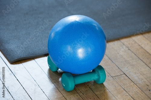 pilates exercise therapy ball on 3 pound hand held weights on wooden floor, next to yoga mat