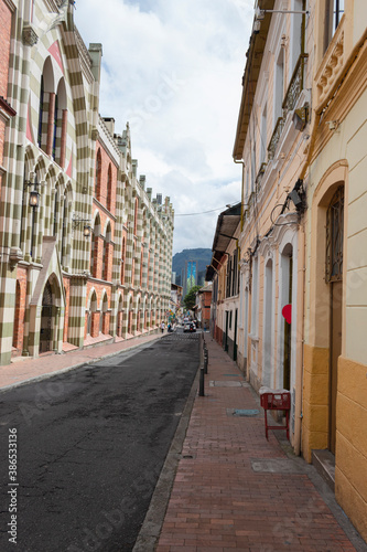 BOGOTA, COLOMBIA La Candelaria, a famous colonial neighborhood street with colored houses and modern skyscraper at background with cloudy sky