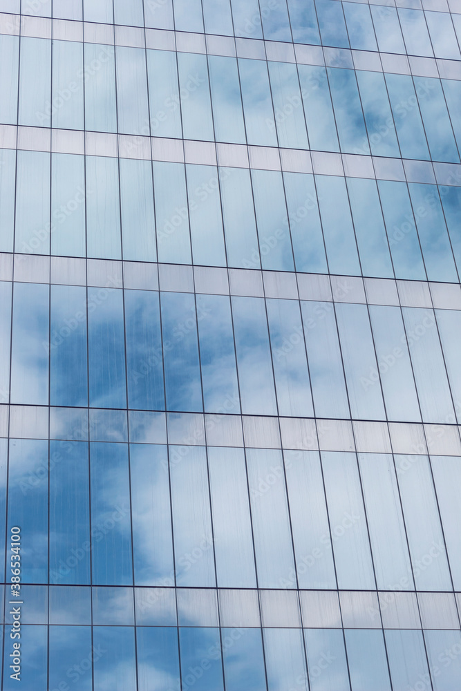 Obraz premium Closeup to a blue cloudy sky reflecting on a modern skyscraper window. Symmetry and architecture concept