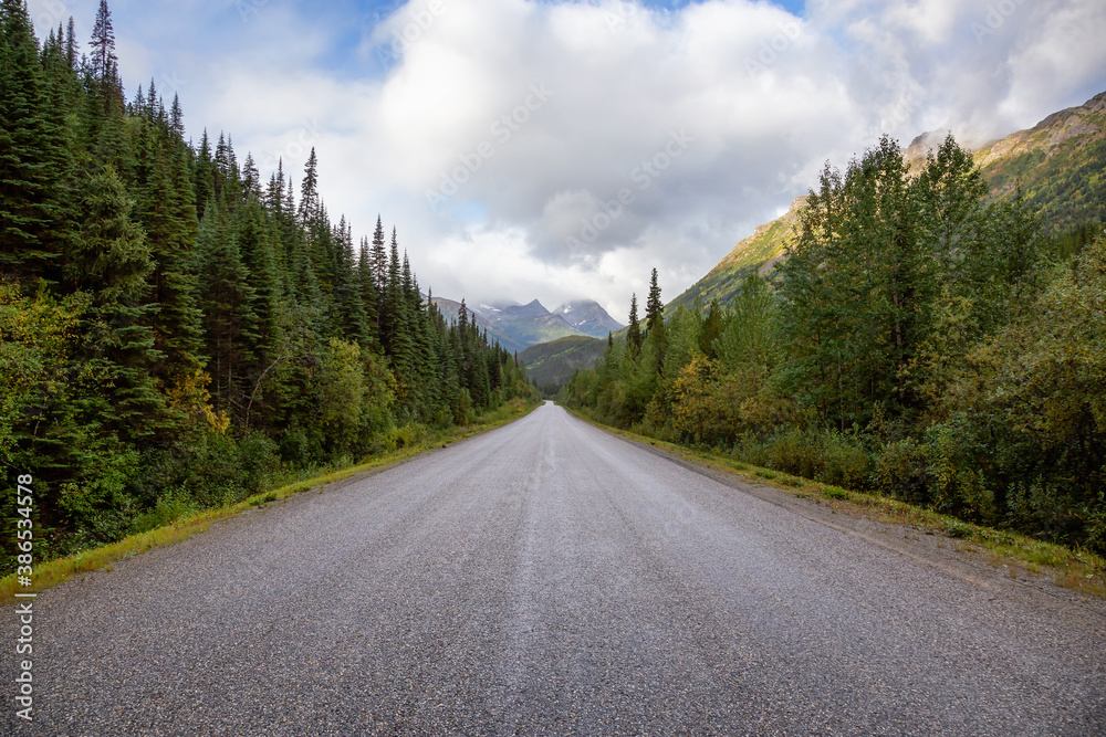 View of Scenic Road surrounded by Trees and Mountains on a Cloudy Fall Morning in Canadian Nature. Taken in Northern British Columbia, Canada. View of Scenic Road surrounded by Trees and Mountains on a Cloudy Fall Morning in Canadian Nature. Taken in Northern British Columbia, Canada.