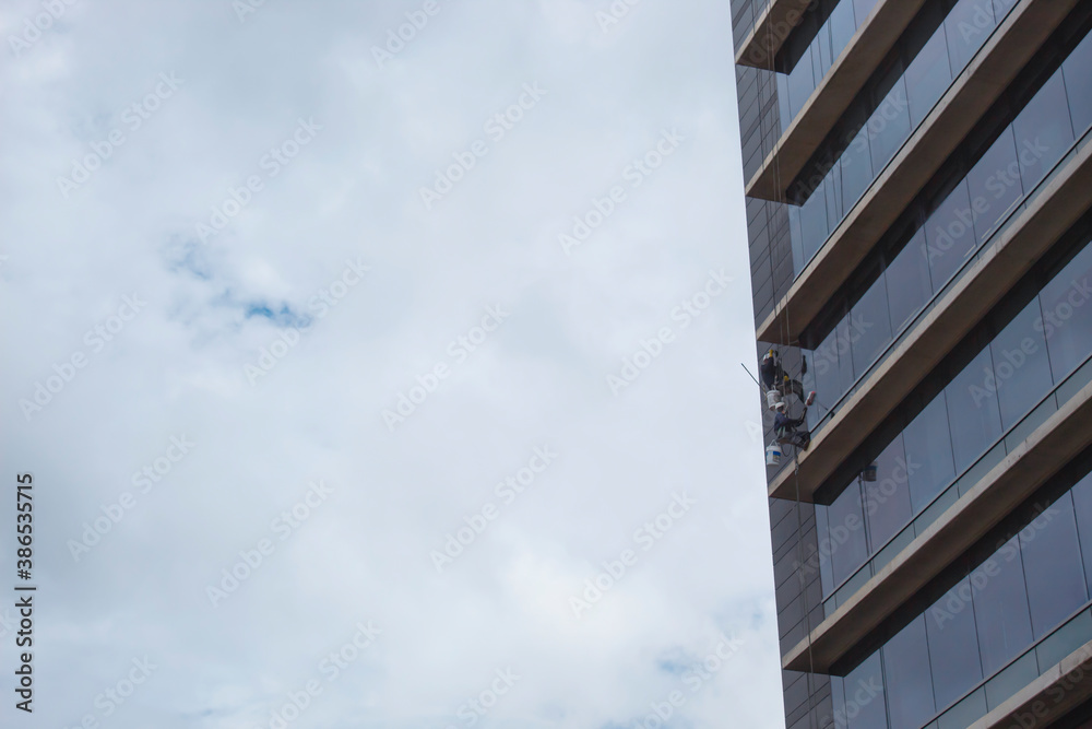 A windows washer doing his risky job at moder building with blue windows and blue cloudy sky at background. 