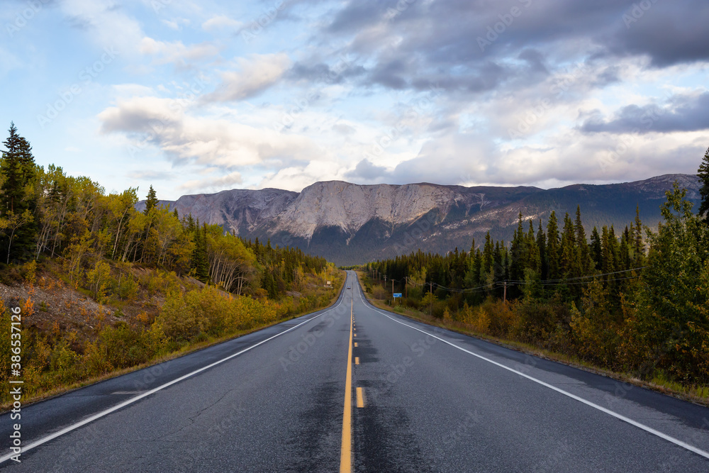 View of Scenic Road surrounded by Trees and Rocky Mountains on a Cloudy Fall Day in Canadian Nature. Taken near Whitehorse, Yukon, Canada. View of Scenic Road surrounded by Trees and Rocky Mountains on a Cloudy Fall Day in Canadian Nature. Taken near Whitehorse, Yukon, Canada.