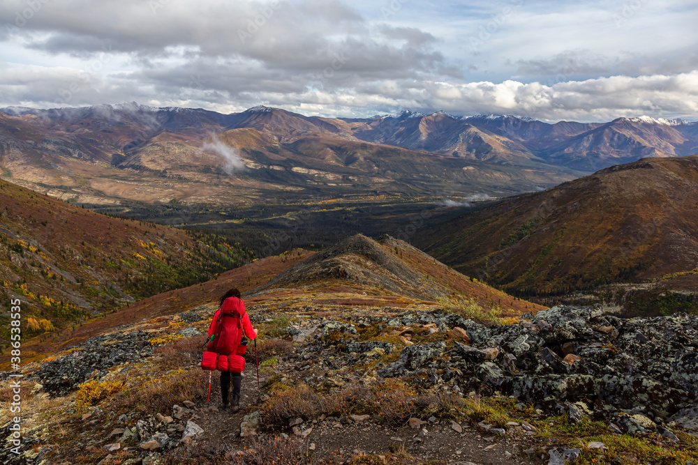 Woman Backpacking along Scenic Hiking Trail surrounded by Mountains in Canadian Nature. Taken in Tombstone Territorial Park, Yukon, Canada.
