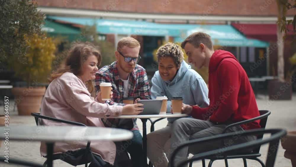 Diverse group of happy friends using digital tablet drinking takeaway coffee at street cafe Diverse group of happy friends using digital tablet drinking takeaway coffee at street cafe
