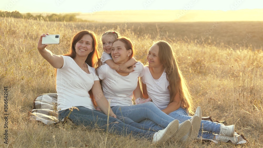 happy family travels, selfie on smartphone in park. mom and healthy children are sitting on blanket. mother with her daughters is photographed in field on blanket. family travel and adventure concept