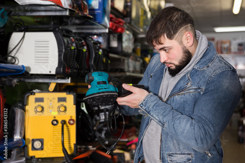 Confident man choosing electric vibratory surface grinder in tools store