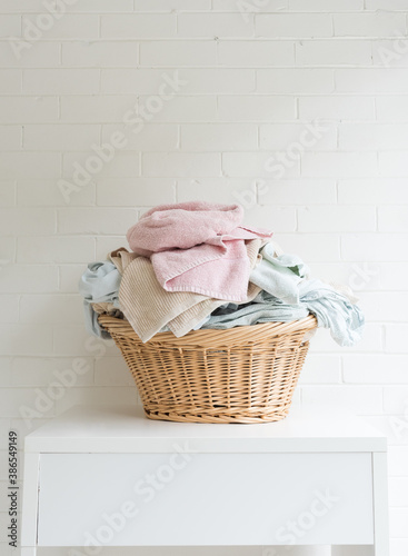 Vertical view of pink towel and blue sheets in wicker laundry basket on white table against painted brick wall (selective focus)