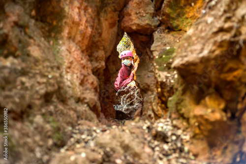 A teenage girl wearing a protective mask peeps through a crack in a rock. Concept of hiking in Pandemia covid 19 