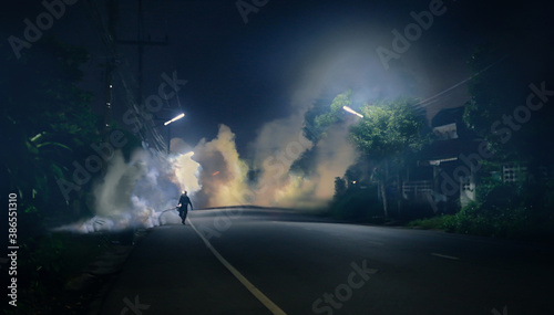 Man using fogging machine to kill mosquitoes with plenty of smoke on public area and shooting into culvert at roadside to prevent malaria