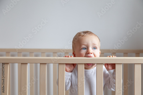 Blond cute little baby biting wooden bed headboard