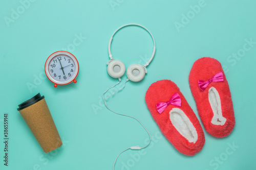 Slippers, a glass of coffee, an alarm clock and headphones on a blue background.