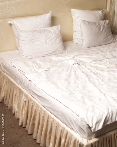 Sleeping bed interior with beige textile, white duvet and four pillows. Bed maid-up with clean white pillows and bed sheets in beauty room. Close-up