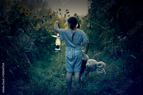 Fairytale, halloween concept with small girl walking in the night with lantern and her teddy