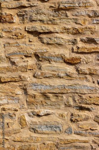 Full frame abstract texture background of a shabby chic antique tan color rugged stone wall with natural stones and thick cement mortar