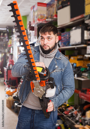 Portrait of adult man with an electric brush cutter in hardware store