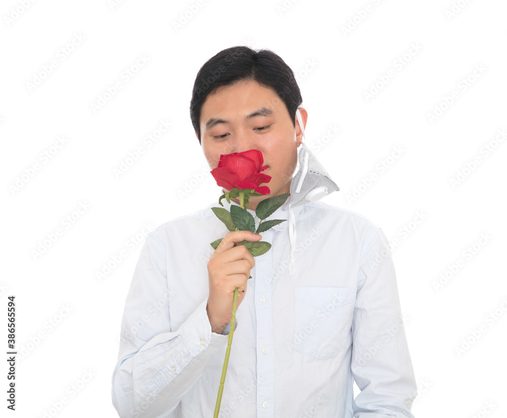 Man takes off mask to smell red rose in front of white background Man takes off mask to smell red rose in front of white background