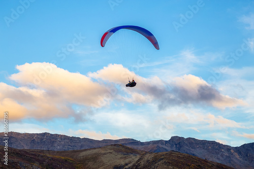 Paraglider flying over Scenic Mountain Range, surrounded by Clouds in Canadian Nature. Taken in Tombstone Territorial Park, Yukon, Canada.