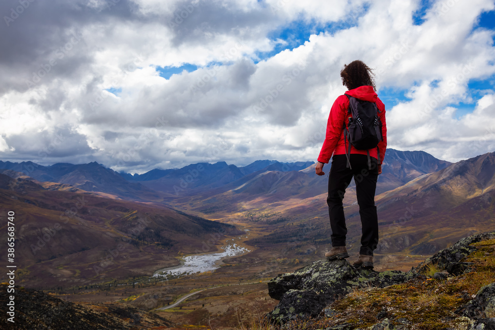 Woman Standing and Looking at Scenic Road and Mountain Range on a Cloudy Fall Day in Canadian Nature. Taken in Tombstone Territorial Park, Yukon, Canada.
