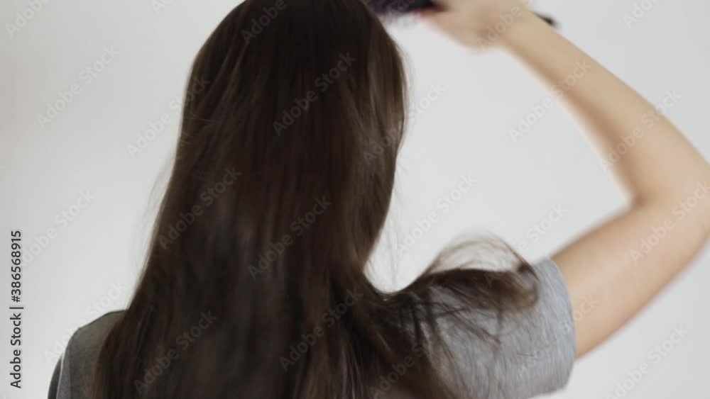 The girl combs her hair. Close up. On a gray background. The girl combs her hair. Close up. On a gray background.