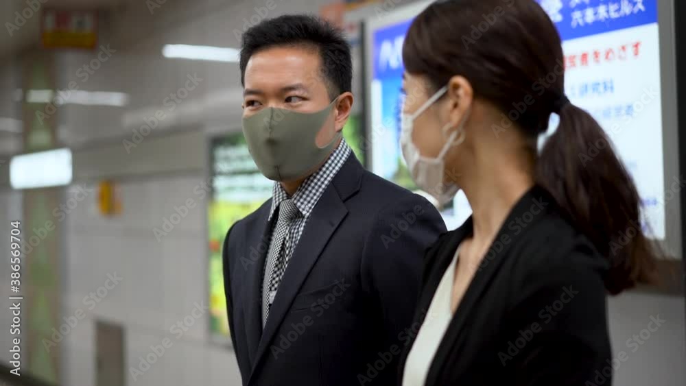 Japanese business man and woman wearing face mask talk while waiting in subway station. Japanese business man and woman wearing face mask talk while waiting in subway station.