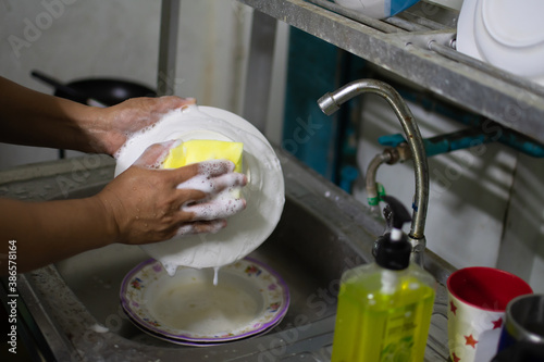 Close up and selective focus on the hands of a woman washing dishes and Remove stains with dishwashing liquid in the kitchen After dinner. blurred background.