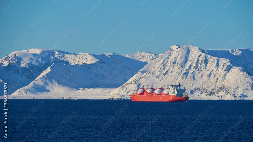 Big red painted LNG (liquefied natural gas) carrier vessel lying at anchor in the arctic ocean in front of Sørøya island with snow-covered mountains near Hammerfest, Norway, Scandinavia in winter.