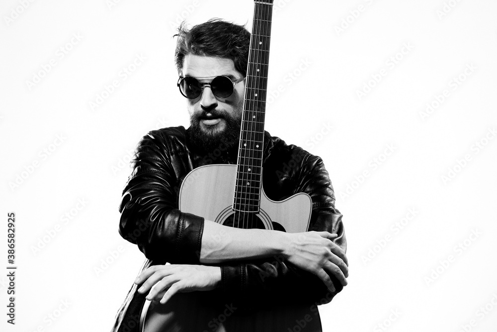 Obraz premium A man holds a guitar in his hands music emotions black leather jacket dark glasses studio light background