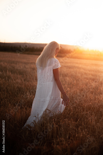  A young blonde girl stands in a field and looks at the sunset. Village life, slow living 